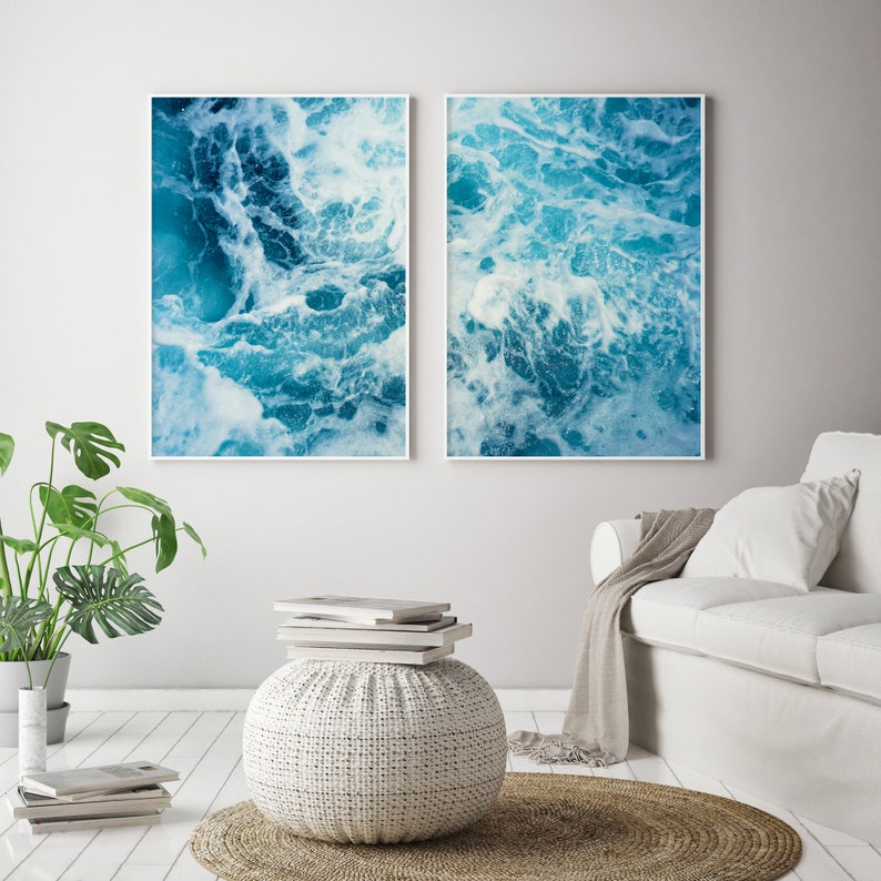 May include: Two framed wall art prints featuring abstract ocean wave patterns in shades of blue and white. The artwork captures the movement and texture of water, creating a calming and natural aesthetic. The prints are displayed in a modern living space.