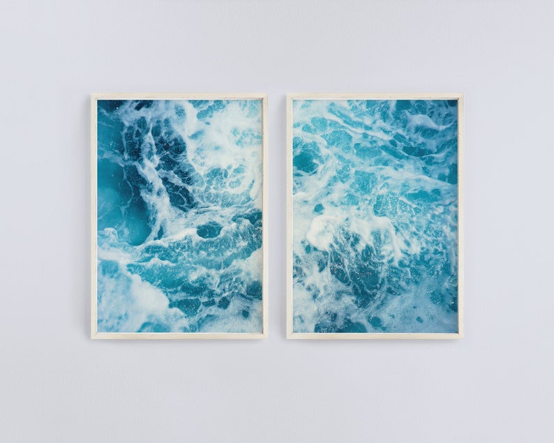 May include: Two framed art prints featuring a close-up view of ocean water. The water is a vibrant turquoise color with white foam and churning waves. The frames are a light beige color, and the art is displayed against a white wall.