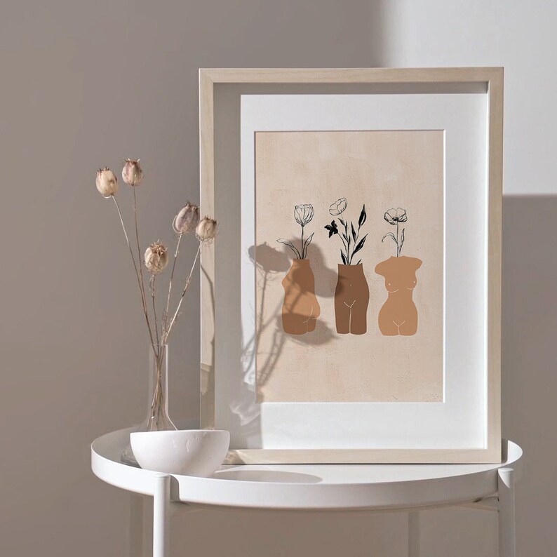 Pu&ograve; includere: Una stampa incorniciata con un design minimalista che presenta tre figure femminili stilizzate con fiori che crescono dalle loro teste. Le figure sono delineate in nero e riempite con un colore marrone chiaro. Lo sfondo &egrave; beige chiaro.