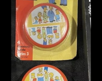 May include: Set of four yellow and red round coasters featuring the Simpsons family. The coasters show the family in two different time periods, "Then" and "Now". The text "The Simpsons 300th Episode" is on the packaging.