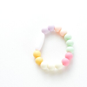 May include: A pastel-coloured beaded bracelet with a variety of beads. The bracelet features beads in shades of yellow, orange, pink, green, and purple. The bracelet is set against a white background.