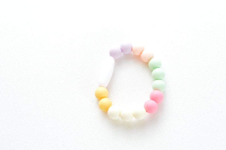 May include: A pastel-coloured beaded bracelet with a variety of beads. The bracelet features beads in shades of yellow, orange, pink, green, and purple. The bracelet is set against a white background.