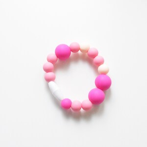 May include: A bracelet made of pink and white beads. The bracelet has a variety of round beads in shades of pink and white, with a white clasp. The beads vary in size, with some larger, brighter pink beads interspersed.