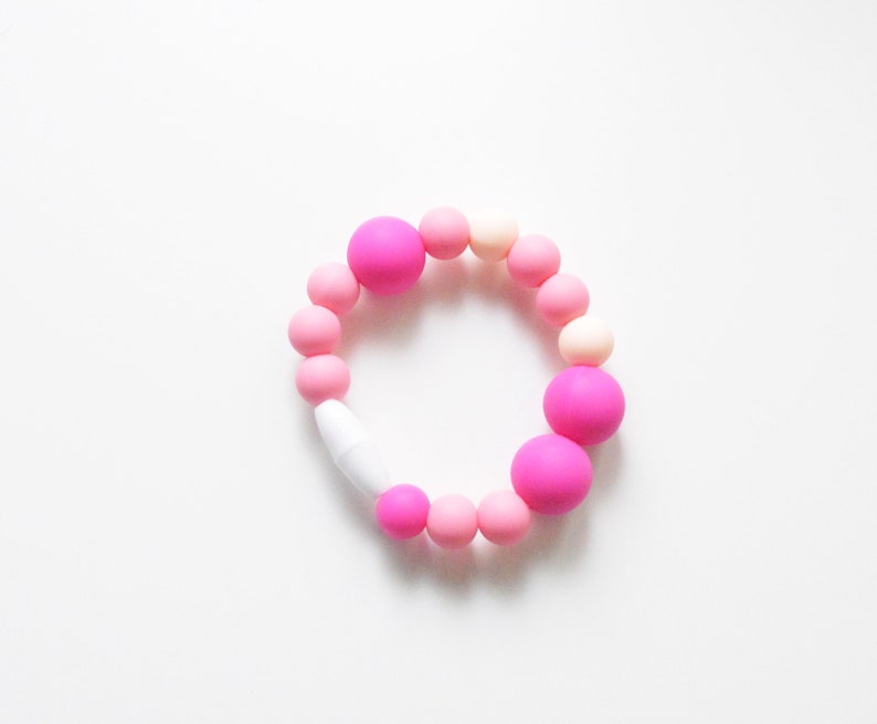 May include: A bracelet made of pink and white beads. The bracelet has a variety of round beads in shades of pink and white, with a white clasp. The beads vary in size, with some larger, brighter pink beads interspersed.