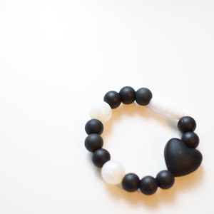 May include: A black and white beaded bracelet with a heart-shaped charm. The bracelet features black and white round beads and a black heart-shaped charm. The bracelet is approximately 18 cm in circumference.