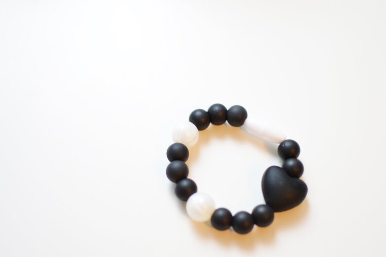May include: A black and white beaded bracelet with a heart-shaped charm. The bracelet features black and white round beads and a black heart-shaped charm. The bracelet is approximately 18 cm in circumference.