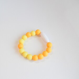 May include: A bracelet with yellow and orange beads, changing in colour. The bracelet is fastened with a white clasp. The beads are arranged in a circular shape.