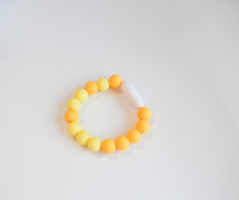 May include: A bracelet with yellow and orange beads, changing in colour. The bracelet is fastened with a white clasp. The beads are arranged in a circular shape.