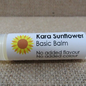 May include: A clear lip balm tube with a white label featuring a sunflower graphic and the text "Kara Sunflower Basic Balm". The balm is labeled "No added flavour" and "No added colour".