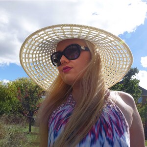 May include: A woman wearing a white crochet sun hat with a black and white geometric pattern. She is wearing sunglasses and a colorful halter top.