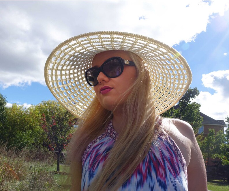 May include: A woman wearing a white crochet sun hat with a black and white geometric pattern. She is wearing sunglasses and a colorful halter top.