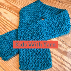 Puede incluir: Bufanda de punto de color turquesa con un patrón texturizado. La bufanda está hecha de hilo grueso y está doblada sobre una superficie de madera. El texto "Kids With Yarn" se muestra en un rectángulo rojo.