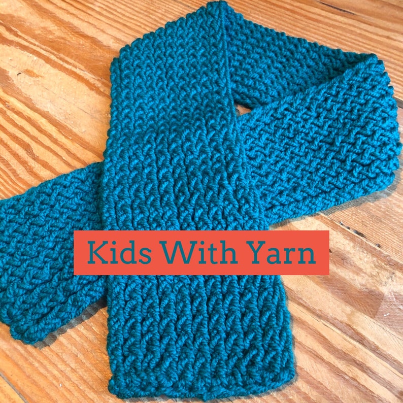 Puede incluir: Bufanda de punto de color turquesa con un patr&oacute;n texturizado. La bufanda est&aacute; hecha de hilo grueso y est&aacute; doblada sobre una superficie de madera. El texto "Kids With Yarn" se muestra en un rect&aacute;ngulo rojo.
