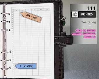 May include: A black leather planner open to a yearly log sheet. The log sheet has a grid layout with labels for months and days. The text "JAN - DEC" and "1 - 31 days" are on the sheet. A printed label reads "Yearly Log".