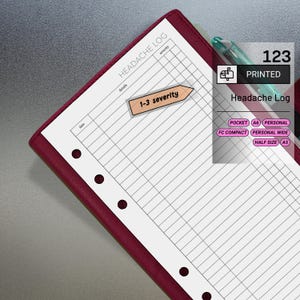 May include: A printed headache log with a burgundy leather cover. The log includes sections for details, severity, and date. A small, light brown arrow-shaped sticker reads "1-3 severity". A pen rests on the page.
