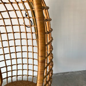 May include: A woven wicker hanging chair with a natural brown finish. The chair has a rounded, egg-shaped design and is suspended by a chain.
