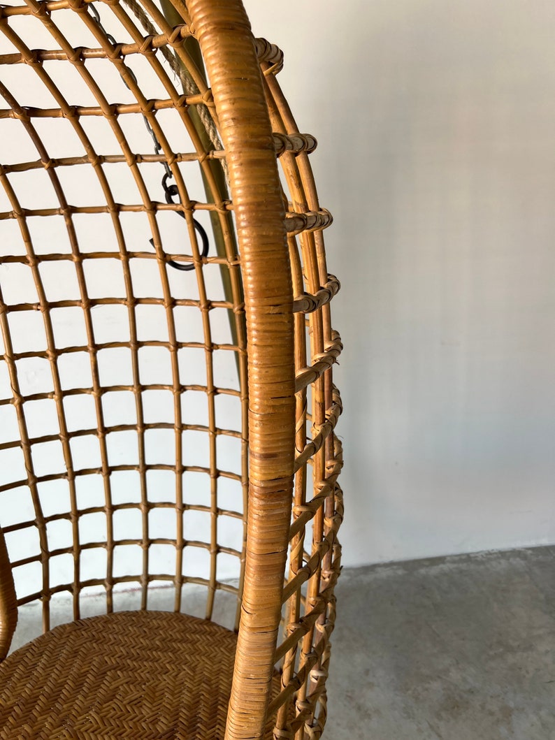May include: A woven wicker hanging chair with a natural brown finish. The chair has a rounded, egg-shaped design and is suspended by a chain.