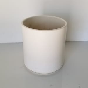 May include: A white ceramic planter with a cylindrical shape. The planter is smooth and has a matte finish.