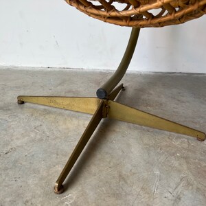 May include: A gold metal base with three legs supports a wicker egg chair. The base has a black rubber foot at each leg.