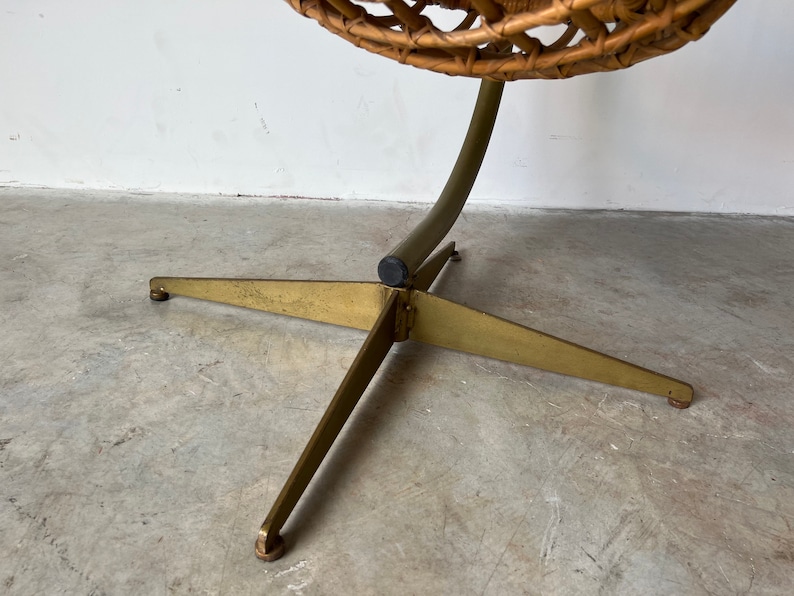 May include: A gold metal base with three legs supports a wicker egg chair. The base has a black rubber foot at each leg.