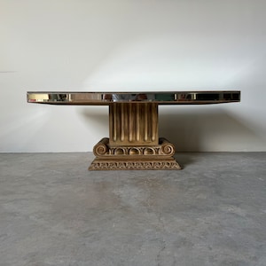 May include: A large, oval, mirrored coffee table with a gold-painted, ornate, column-style base.