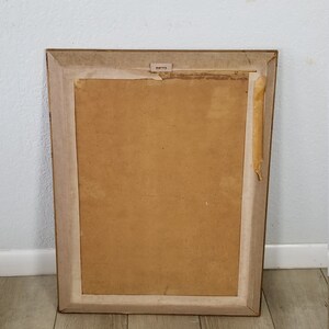 May include: A brown wooden picture frame with a light brown mat and a piece of tape on the right side.