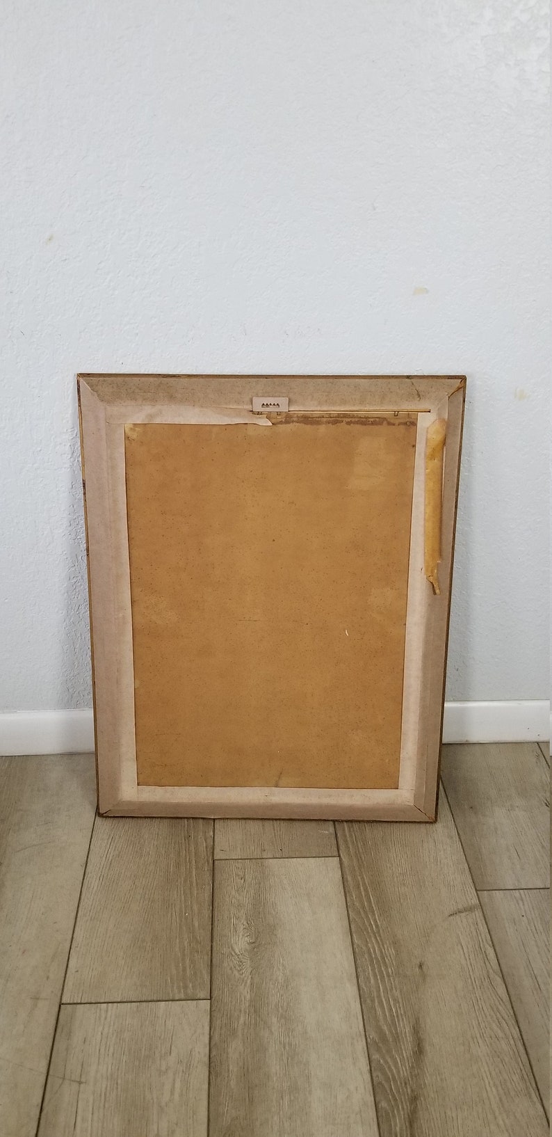 May include: A brown wooden picture frame with a light brown mat and a piece of tape on the right side.