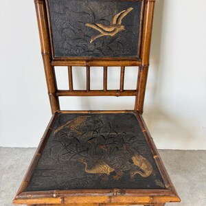 May include: A vintage bamboo chair with a dark seat and back featuring embossed bird designs in gold and brown. The chair has a natural wood finish and a classic, elegant design, suitable for home decor.