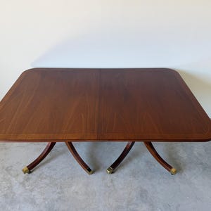 May include: A rectangular wooden dining table with a rich brown finish and a visible grain pattern. The table features a smooth surface with rounded corners and is supported by four curved legs that terminate in metallic brass-colored feet.