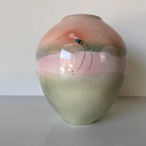 May include: A ceramic vase with a rounded shape, featuring a gradient of colors from light green at the base to pink and peach at the top. The vase is decorated with a minimalist floral design and small black dots.