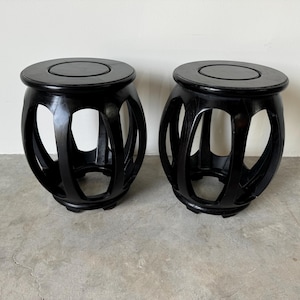 May include: Two black wooden stools with a round top and an open, circular design. The stools are made of dark wood and have a smooth finish.