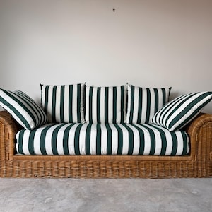 May include: A natural light brown woven wicker sofa featuring rolled arms and a thick seat cushion. The sofa includes three square back cushions and two side cushions, all upholstered in a white fabric with vertical dark green stripes.