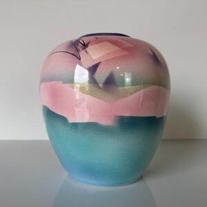 May include: A small, round ceramic vase with a pink, blue, and yellow abstract design. The vase has a glossy finish.