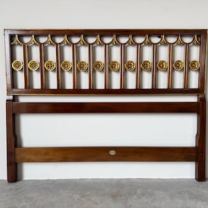 May include: A dark brown wooden headboard with gold accents. The headboard features a rectangular frame with vertical bars and decorative gold medallions. The top has a decorative gold trim. A classic piece of bedroom furniture.