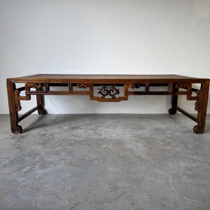 May include: A long, rectangular, dark wood coffee table with intricate carvings on the legs and apron. The table has a simple, rectangular top and a traditional Chinese design.
