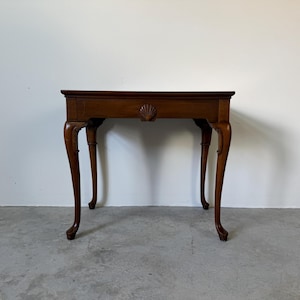 May include: A small, antique wooden table with a dark brown finish. The table features a rectangular top, a carved shell design, and four curved legs. The table is approximately 30 inches long, 18 inches wide, and 28 inches high.