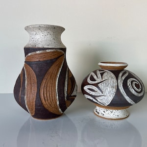 May include: Two ceramic vases with abstract designs. The larger vase is brown with white and brown geometric patterns. The smaller vase is brown with white and brown swirling patterns.
