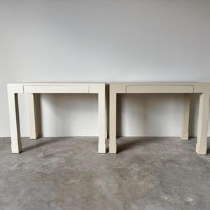 May include: Two white rectangular tables with a single drawer each. The tables have a simple design with square legs.