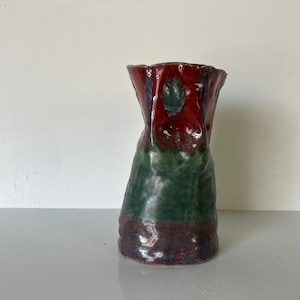 May include: A hand-crafted ceramic vase with a unique, textured surface. The vase is glazed in shades of red, green, and blue.