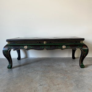 May include: A black and green coffee table with a marble top and intricate floral designs. The table has four legs with a curved design.