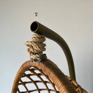 May include: Close-up of the top of a hanging wicker chair with a metal frame and rope hanging system.