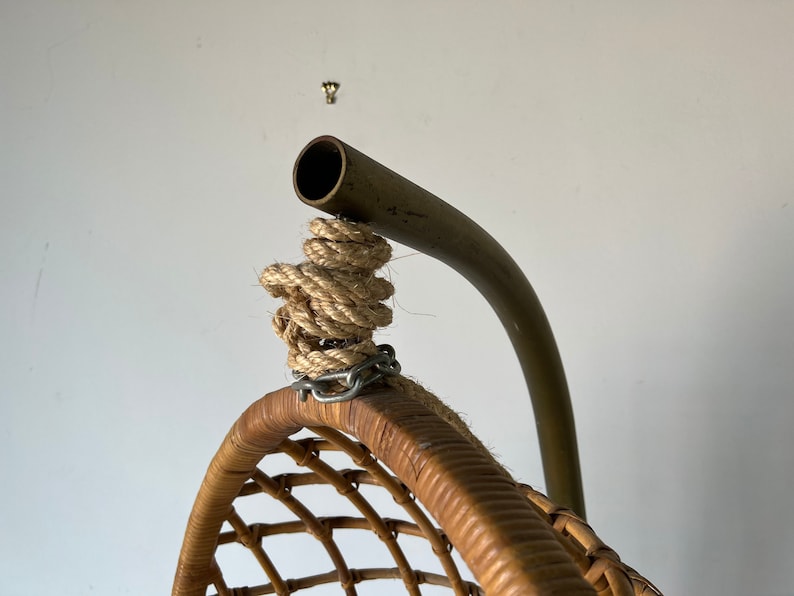 May include: Close-up of the top of a hanging wicker chair with a metal frame and rope hanging system.