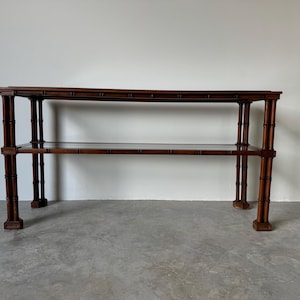 May include: A brown wooden console table with two shelves and a glass top. The table has a simple, elegant design and is perfect for displaying decorative items or storing books.