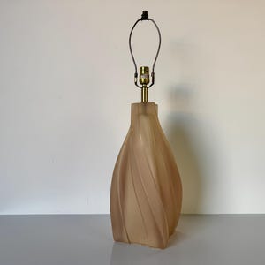 May include: A beige ceramic table lamp with a twisted, organic shape. The lamp has a simple metal shade and a gold-toned socket.
