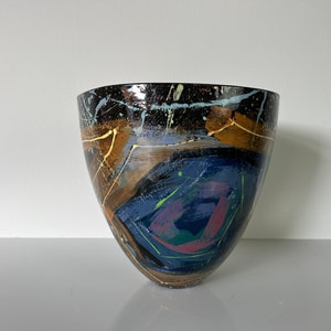 May include: A ceramic bowl with an abstract design in shades of blue, brown, yellow, green, and pink. The bowl has a wide, rounded opening and a narrow base.