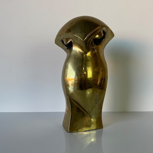 May include: A gold-colored abstract sculpture with a rounded top and a curved, elongated body. The sculpture has a smooth, polished finish.