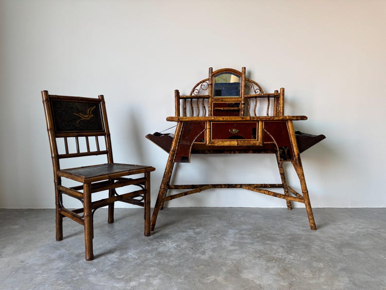 May include: Antique bamboo desk and chair set. The desk features a red and gold finish with a mirror and drawers. The chair has a dark seat and back with a decorative design. A unique vintage furniture set.
