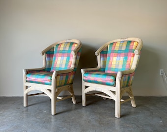 May include: Two white wicker chairs with colorful plaid upholstery. The chairs have a high back and a curved armrest.