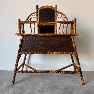 May include: An antique bamboo desk with a dark brown, textured surface. The desk has a high back with a decorative arch and a small mirror. The frame is made of bamboo with a natural finish.