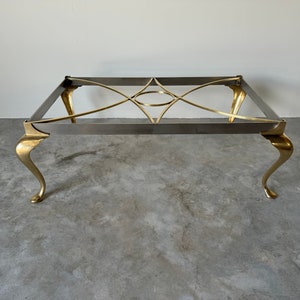 May include: A brass and silver coffee table with a geometric design. The table has four legs with a claw foot design.